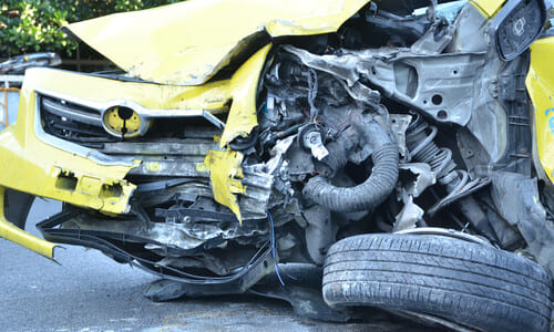 A totaled yellow car on the side of a road after a serious accident.