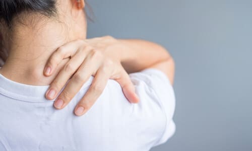 An accident victim in a white shirt reaching for the back of her neck due to neck pain.