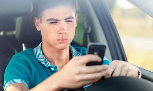 A young driver looking at his phone while behind the wheel of his car.