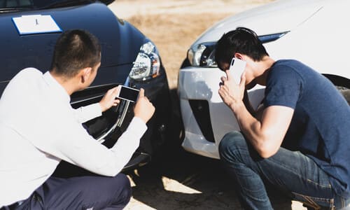 Two men documenting their vehicle accident on their phones.