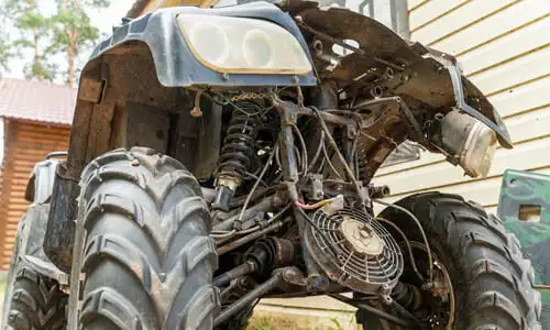 A low-to-the-ground shot of a dirty, worn-down ATV outside a garage door.