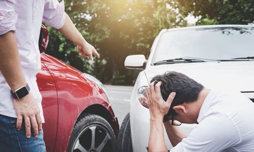 Two drivers arguing after a collision between their red and white vehicles.