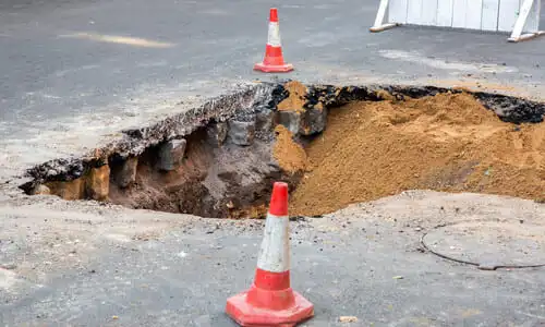 A demolished segment of roadway in a city with traffic cones warning of it.