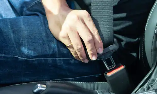 A closeup of a person fastening their seatbelt before a car starts.