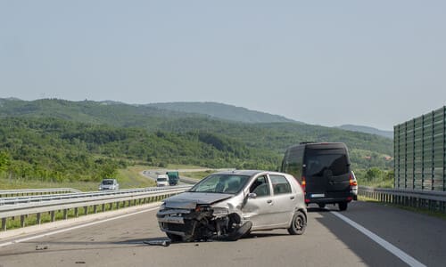 An accident on a highway between a silver-grey hatchback and a black van.