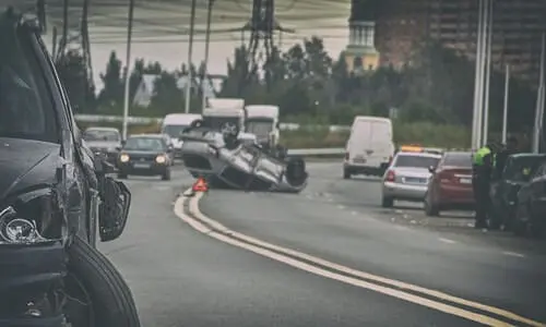 An overturned silver grey sedan on a major national road on a late afternoon.