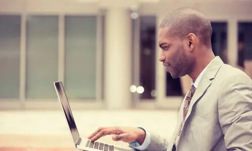 A side shot of a left turn accident lawyer reviewing a client's case on his laptop outside a building.