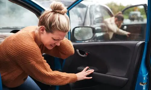 A car passenger stepping out of a car and grasping her neck in pain after a collision.