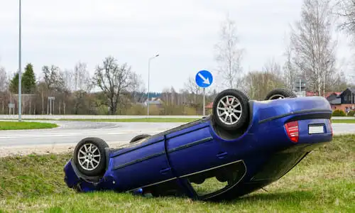 A blue car flipped over and forced off road after an accident with another car.