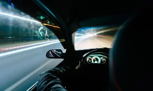 An over the shoulder shot of a man speeding at night on a city road.