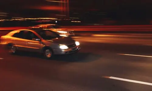 A motion-blurred image of two cars racing each other on a city street at night.