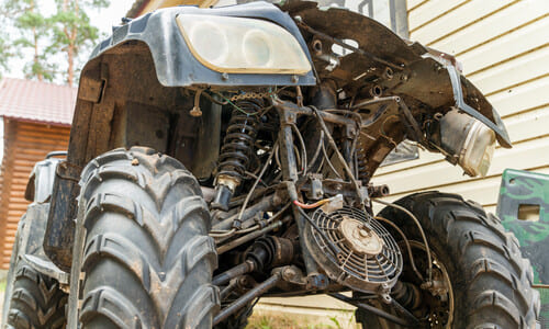 An broken down ATV sitting in a driveway behind a house after an accident.