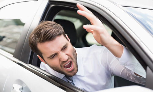 An aggressive driver yelling at another road user in front of him and risking an accident.