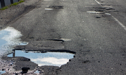 Potholes filled with water on a damaged roadway.