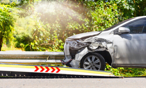 A grey vehicle driving onto a service truck after sustaining damage to its front in an accident.