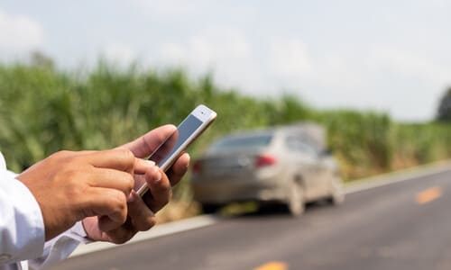 A highway accident victim calling his lawyer on the phone after his car broke down on the road.