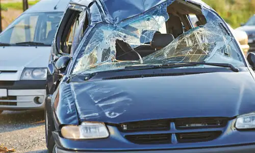 A dark blue car with a broken front end and windshield after an accident with another vehicle.