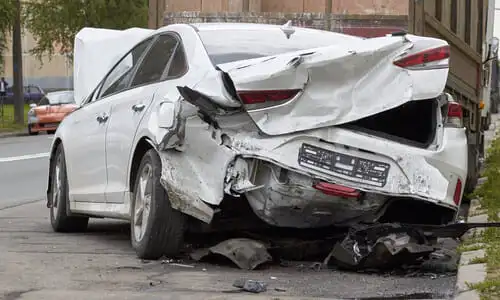 A white car with an open hood and totaled rear end after another vehicle collided while attempting to merge lanes.