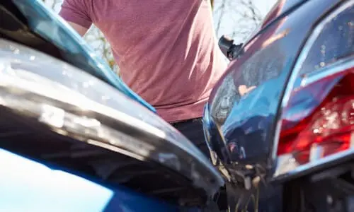 A driver looking at damage caused by a collision between his car and another vehicle in a parking lot.