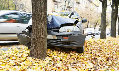 A dark blue car sedan crashed into a tree after having been forced off the road by an aggressive driver.