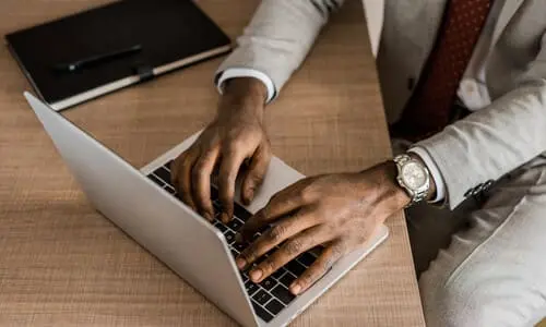 A top-down view of a lawyer's hands working on a client's case on a silver-gray laptop.