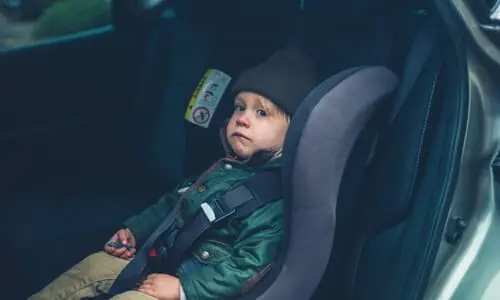 A child in a car seat strapped in with seatbelts and looking nervously out the vehicle.