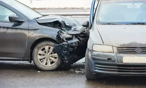 Two dark-colored vehicles in a T-bone accident with each other after one rammed into the other's side at speed.