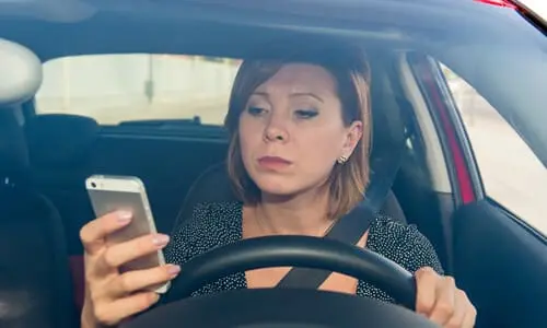 A driver behind the wheel of her car while distracted by a message on her phone.