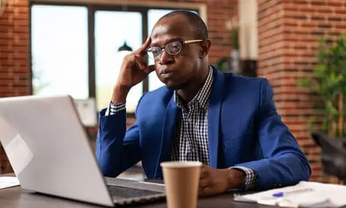 An African-American looking worriedly at his computer realizing he needs help for his claim.