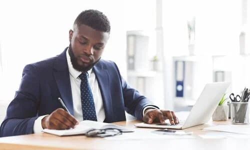 An injury lawyer diligently taking notes and working on his client's case on a laptop in an office.