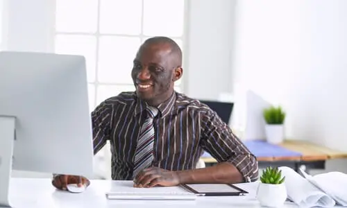 An African-American personal injury lawyer smiling while working on a client's case on his computer.