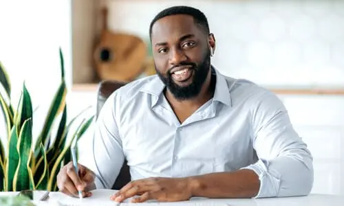 A personal injury lawyer seated at his desk in a well-lit office smiling at the camera