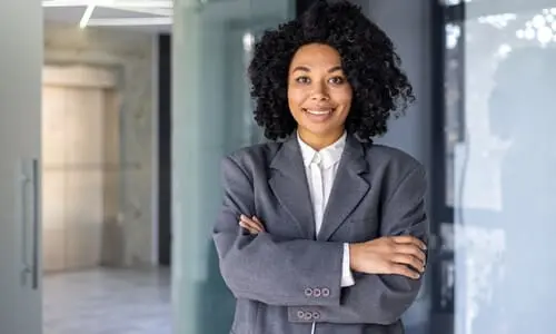 A smiling lawyer standing with crossed arms in front of the glass door entrance to her office.