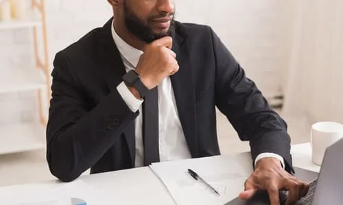 A personal injury attorney with his hand raised to his chin as he works on a client's case on a computer.