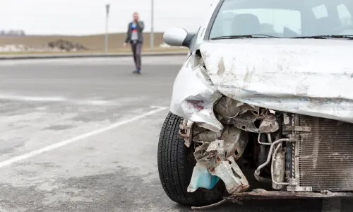 A driver looking at the damage to his car after an uninsured motorist run from the scene.