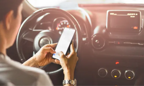 A driver texting with both hands on his phone while behind the wheel of his car.